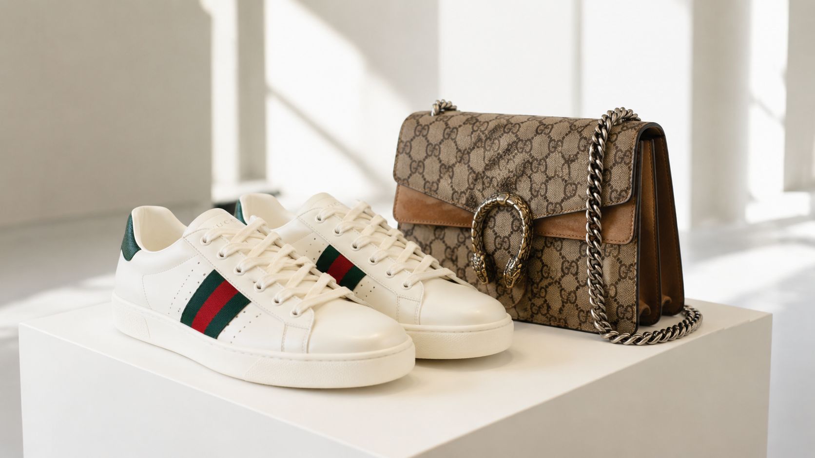 A pair of white Gucci sneakers and a signature Gucci handbag placed on a white pedestal display.