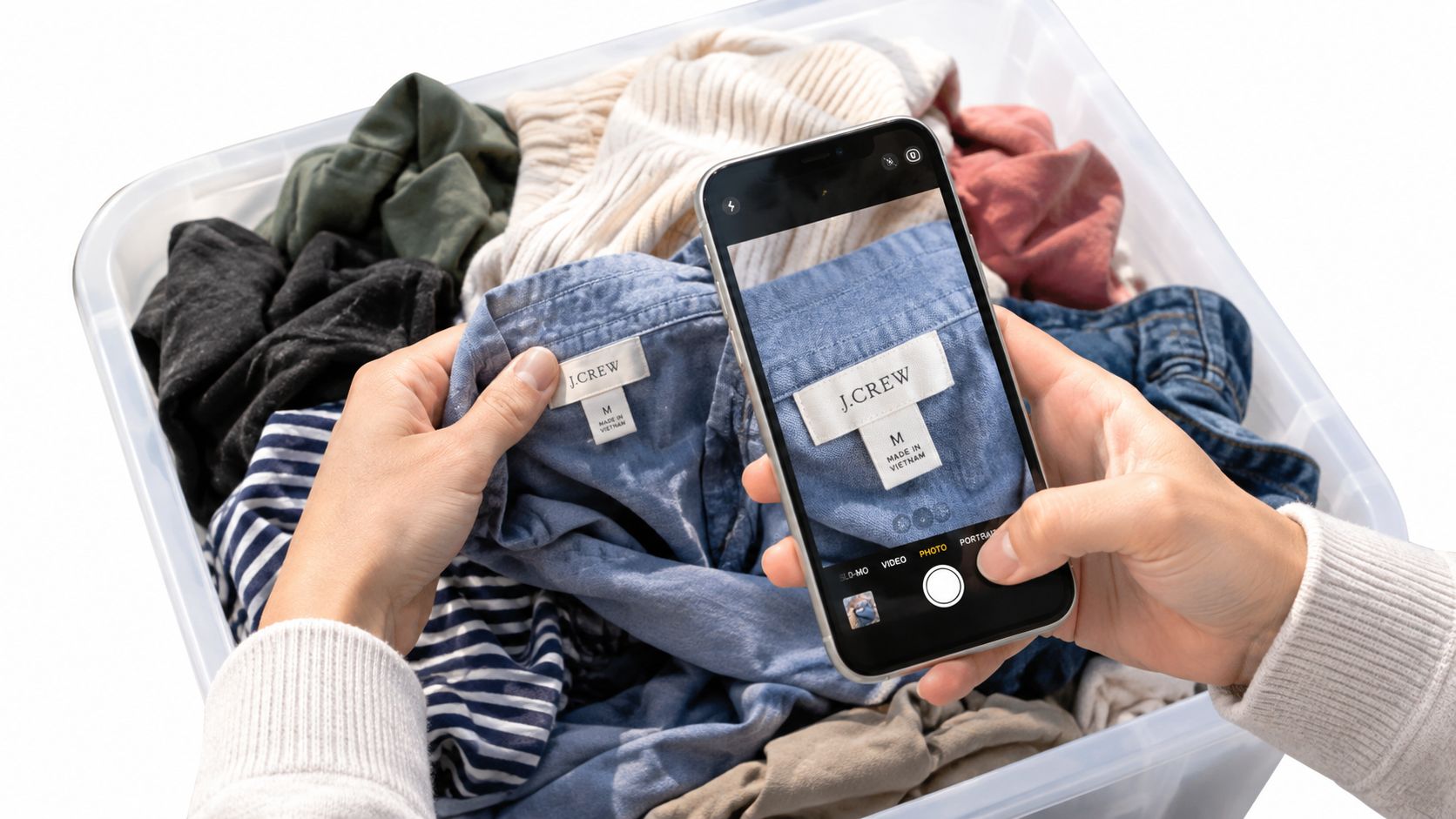 A person uses their smartphone to scan a clothing tag inside a plastic storage bin.